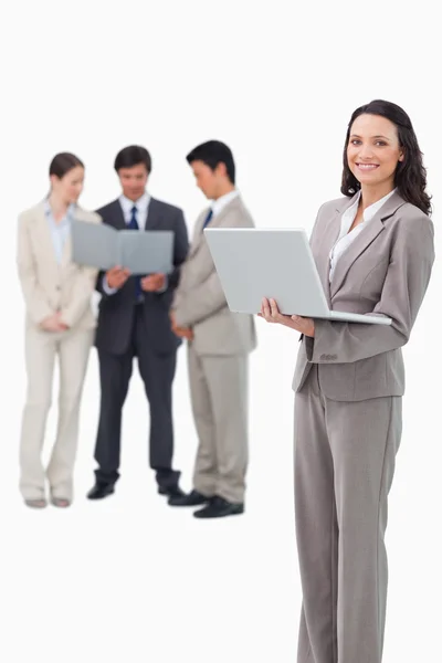 Smiling saleswoman with laptop and associates behind her — Stock Photo, Image