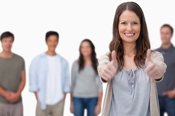 Sorridente donna con gli amici dietro di lei dando pollici in su — Foto Stock