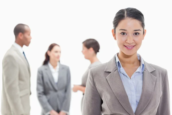 Бізнес-леді посміхається з колегами на задньому плані — стокове фото