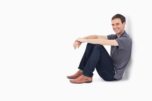 Homem sorrindo enquanto sentado contra uma parede — Fotografia de Stock