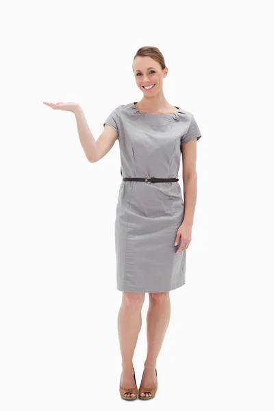 Donna sorridente in un vestito che presenta qualcosa con la mano — Foto Stock