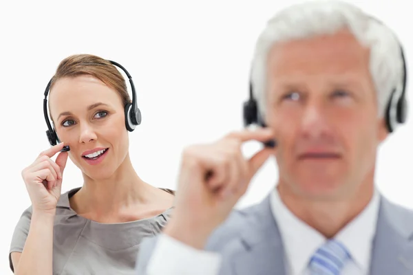 Close-up de uma mulher sorridente falando em segundo plano com um homem de cabelo branco enquanto usava um fone de ouvido contra fundo branco — Fotografia de Stock