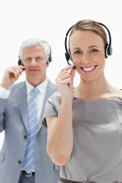Close-up de uma mulher sorridente usando um fone de ouvido com um homem de negócios de cabelo branco no fundo — Fotografia de Stock