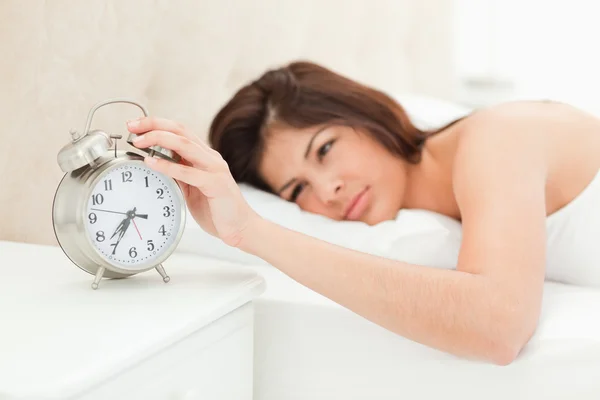 A woman lying in her bed with her hand on the alarm clock, which — Stock Photo, Image