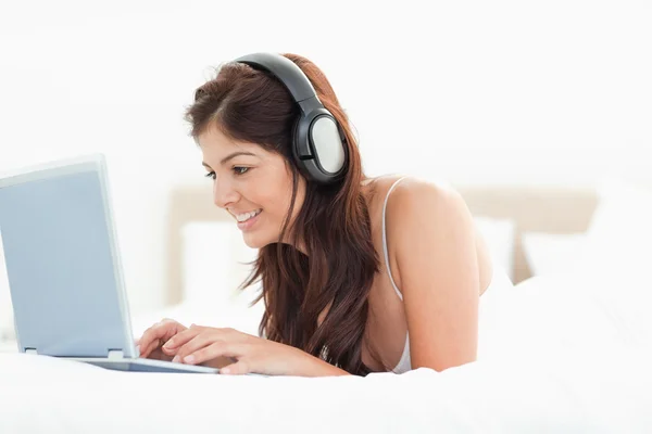 stock image Woman browsing her laptop with headphones while lying on a bed