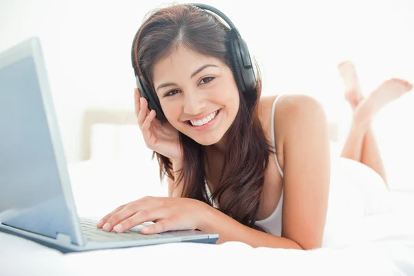 Mulher olhando para a frente sorrindo, enquanto usa um laptop e fones de ouvido — Fotografia de Stock