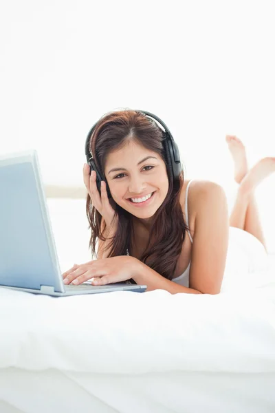Mulher com fones de ouvido e um laptop deitado na cama, ansioso — Fotografia de Stock