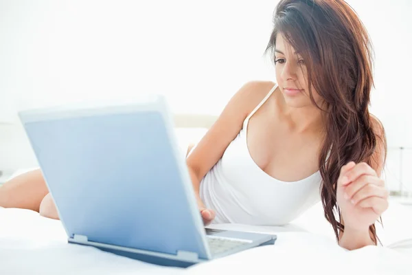 Kvinna ligga uppåt över sängen medan du använder sin laptop — Stockfoto