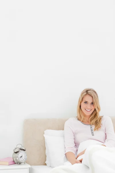 Vertical shot, Woman sitting up against headboard smiling with a — Stock Photo, Image
