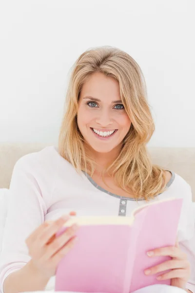 Närbild, kvinnan leende med boken i handen, sitter i sängen — Stockfoto