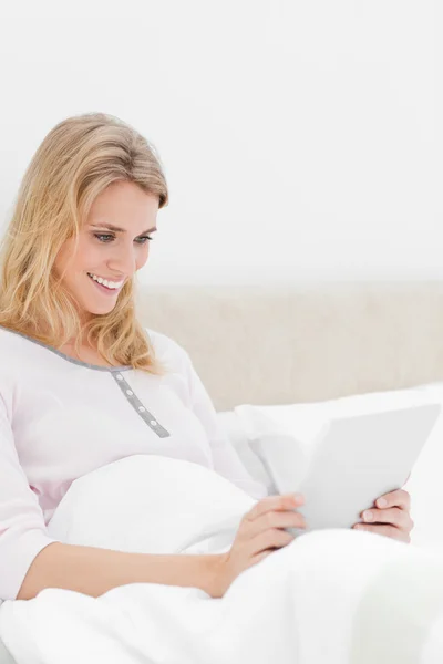Vrouw zitten in bed, met een Tablet PC met beide handen, en smil — Stockfoto