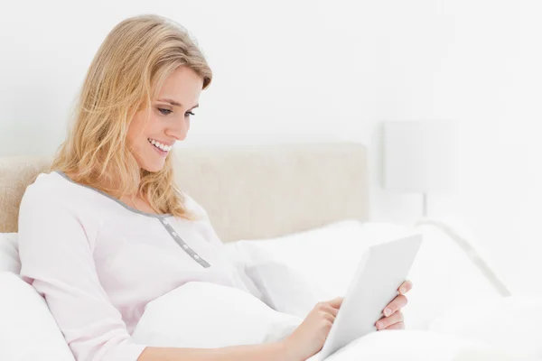 Seitenansicht: Frau sitzt mit Tablet-PC im Bett und lächelt — Stockfoto
