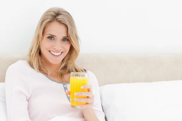 Mulher olhando para a frente e sorrindo com um copo de suco de laranja i — Fotografia de Stock