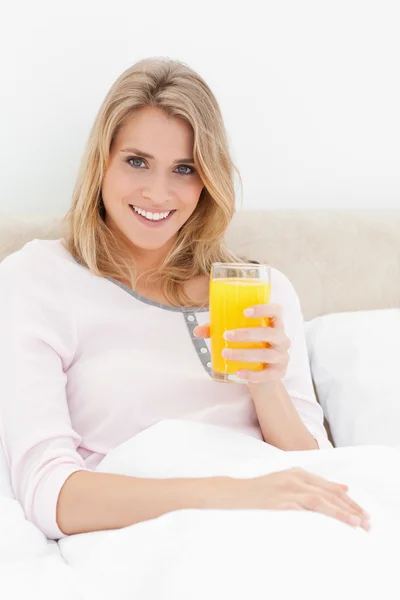 Bliska, kobieta siedziała na łóżku, ze szklanką soku pomarańczowego w — Zdjęcie stockowe
