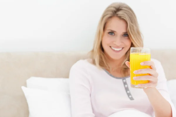 Kobieta trzyma kieliszek soku pomarańczowego, uśmiechając się i patrząc — Zdjęcie stockowe