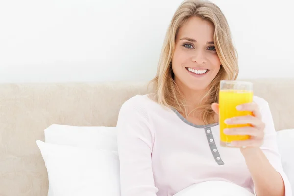 Kvinna med ett glas apelsinjuice medan leende och ser — Stockfoto