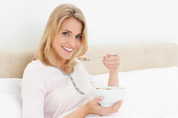 Mujer en la cama con un tazón de cereal en la mano y una cuchara levantada de — Foto de Stock