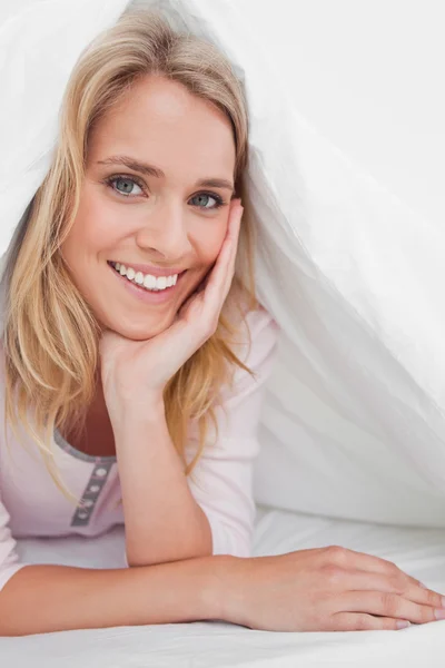 Närbild, kvinnan under täcket leende med hennes hand stödja — Stockfoto