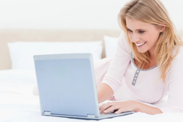女性はベッドに横になっている、ノート パソコンを使用して、笑みを浮かべて — ストック写真