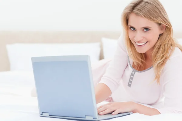Mujer acostada en la cama, con portátil, mirando hacia adelante y sonriendo —  Fotos de Stock