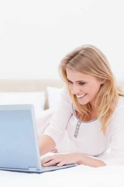 De cerca, Mujer usando un ordenador portátil mientras está en la cama y sonriendo — Foto de Stock