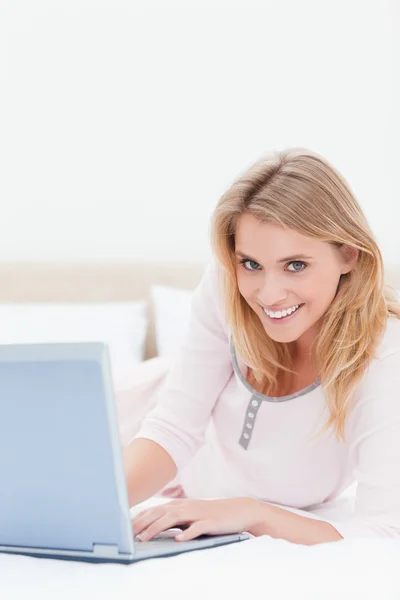 Kvinnan ligger på sängen, med en bärbar dator, medan du tittar framåt och — Stockfoto