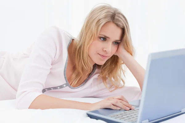 Mujer acostada en la cama desplazándose en su computadora portátil mientras descansa su hea —  Fotos de Stock
