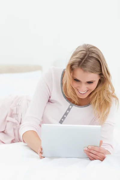 Woman lying across the bed, tablet pc in hand and smiling — Stock Photo, Image