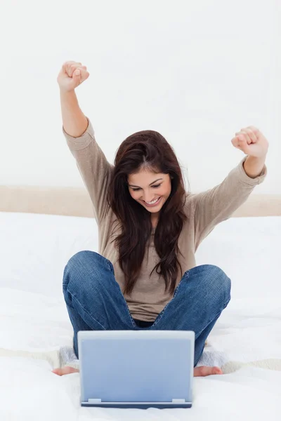 Frau feiert mit in die Luft gereckten Armen, während sie auf ihren Laptop blickt — Stockfoto