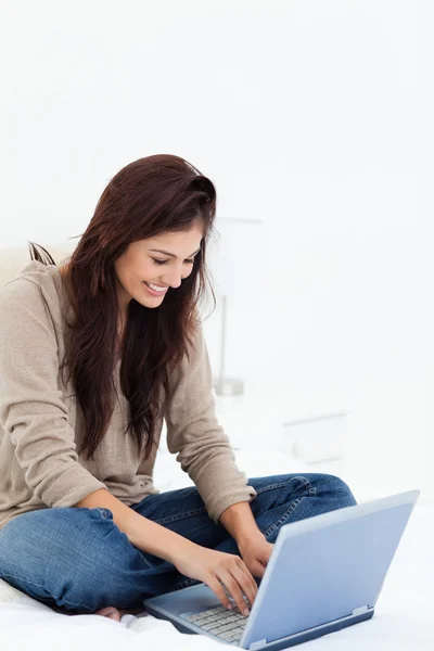 Woman smiling as she uses her laptop on her bed — Stock Photo, Image