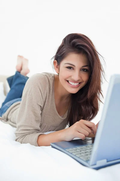 Mulher sorrindo na frente de seu laptop, deitada na cama com ela — Fotografia de Stock