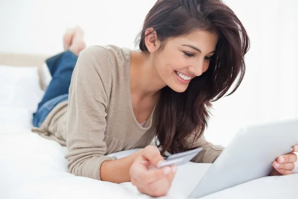 Mulher usando um tablet com seu cartão de crédito, e sorrindo enquanto lyi — Fotografia de Stock