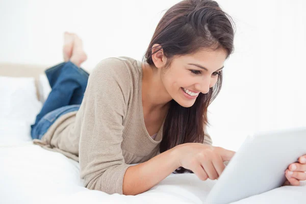 Frau lächelt, während sie auf dem Bett durch ihr Tablet blättert — Stockfoto