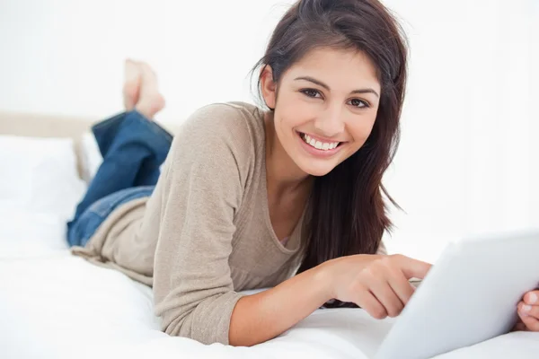 Woman uses tablet as she smiles looking straight ahead, while ly — Stock Photo, Image