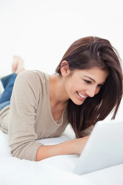 Woman smiling as she uses her tablet while lying on the bed — Stock Photo, Image