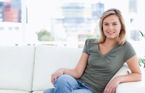 Kobieta uśmiechając się siedząc na kanapie z nogami skrzyżowanymi — Zdjęcie stockowe