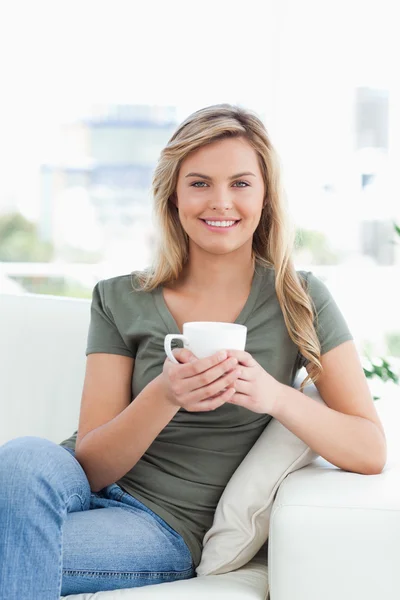 Kvinna med en kopp, leende som hon ser framåt med korsade l — Stockfoto