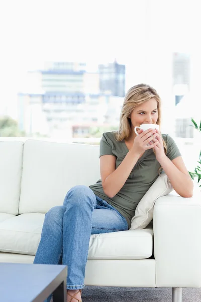 Woman with her legs crossed, holding a mug to her nose and looki — Stock Photo, Image