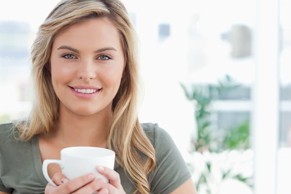 Mulher segurando uma caneca em suas mãos e sorrindo, enquanto olha forw — Fotografia de Stock