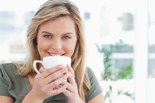 Woman looking forward, smiling with a mug up to near her mouth — Stock Photo, Image
