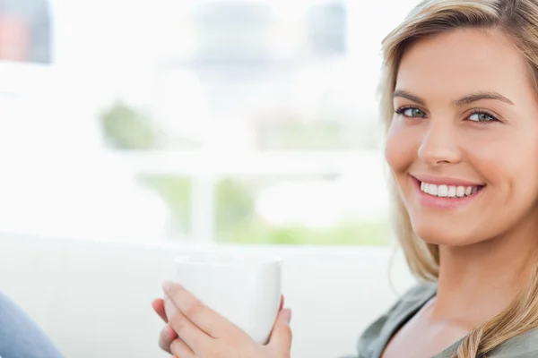 Woman smiling, looking forward and holding up a mug in hands — Stock Photo, Image