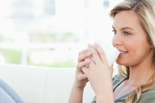 Woman smiling with cup held to her lips and knees raised — Stock Photo, Image