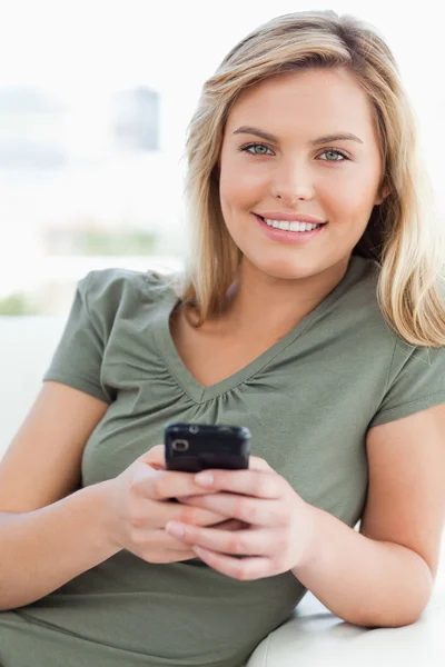 Mujer mirando hacia adelante y sonriendo mientras sostiene su teléfono — Foto de Stock