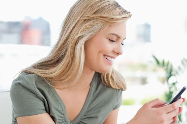 Frau lächelt, während sie ihr Handy in den Händen hält — Stockfoto