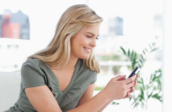 La mujer sonríe mientras usa su teléfono mientras está en el sofá — Foto de Stock