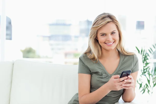 Frau blickt geradeaus und lächelt, während sie ihr Handy benutzt — Stockfoto