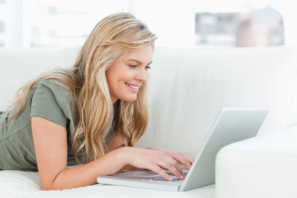 Kobieta uśmiechając się jak ona używa jej laptop leżąc na couc — Zdjęcie stockowe