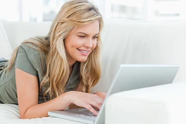 女人躺在沙发上使用她的笔记本电脑和微笑 — 图库照片