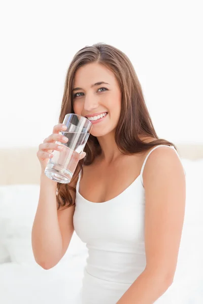 Woman smiles with a glass of water in hand raised to her mouth — Stock Photo, Image