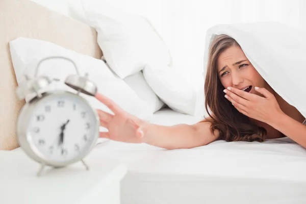The woman yawns while trying to silence her alarm clock — Stock Photo, Image